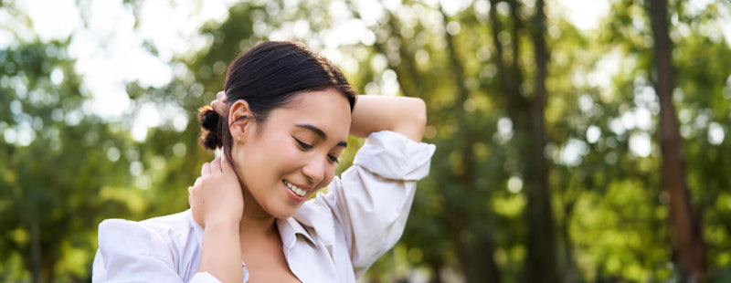 Woman adjusting her hair in a park with greenery in the background