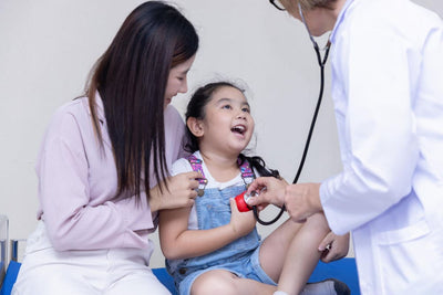 Doctor examining a child with a stethoscope, mother holding the child's hand.