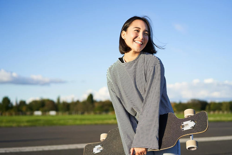 Woman holding a skateboard on a road with a clear sky enjoying life