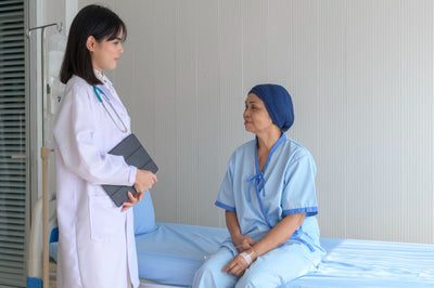 Doctor in white coat talking to a cancer patient in a blue hospital gown.