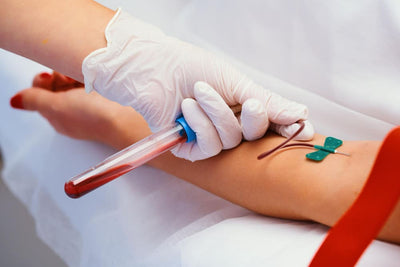 Person receiving a blood sample with gloved hand holding a tube, on a white background