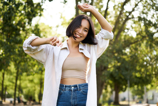 Woman in a white shirt and blue jeans standing outdoors with trees in the background