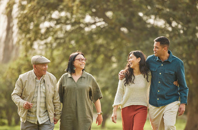 Four people with different age group walking together in a park with trees in the background