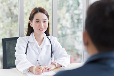 Doctor in a white coat with a stethoscope talking to a patient in an office setting.