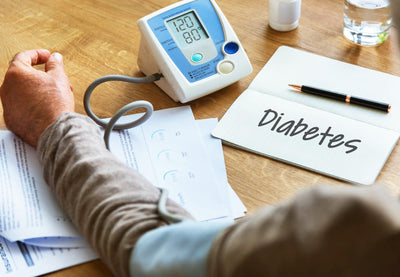 Person checking blood pressure with a digital blood pressure monitor on a table with diabetes notes.