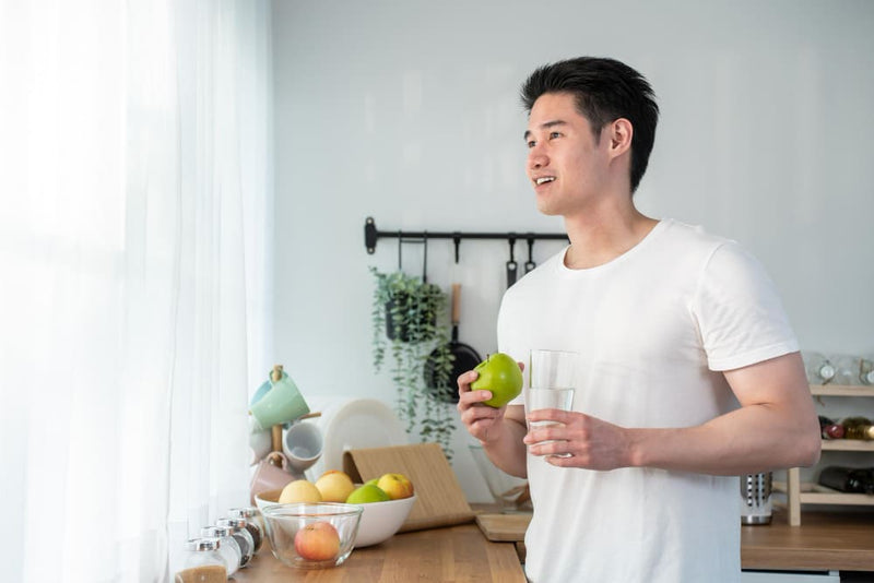 Man holding a glass of water and an apple in a kitchen.