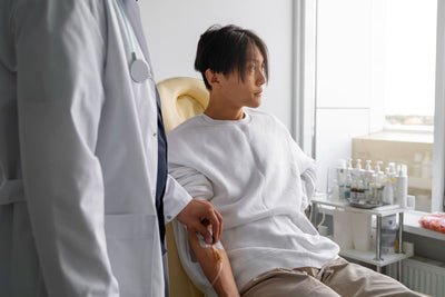Person in a hospital gown sitting in a chair with a medical professional, in a hospital room. Extracting blood sample