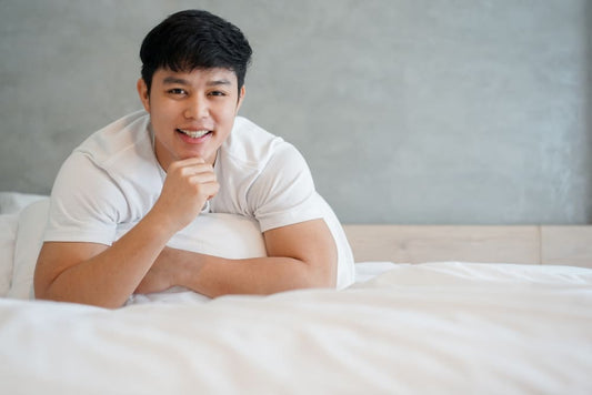 Man lying on a bed wearing a white t-shirt, smiling.