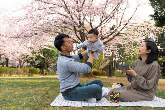 Family of three sitting on a blanket under cherry blossom trees