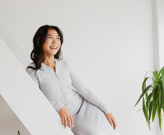 Woman in a gray dress standing indoors with a plant in the corner