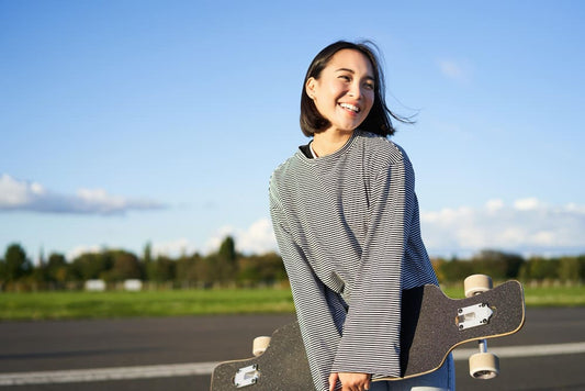 Woman holding a skateboard on a road with a clear sky enjoying life